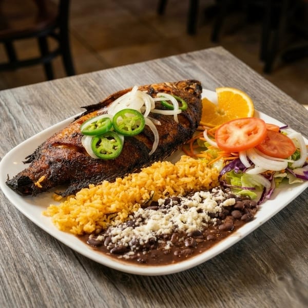 Whole fried fish topped with onions and jalapeños, served with rice, beans, and salad.