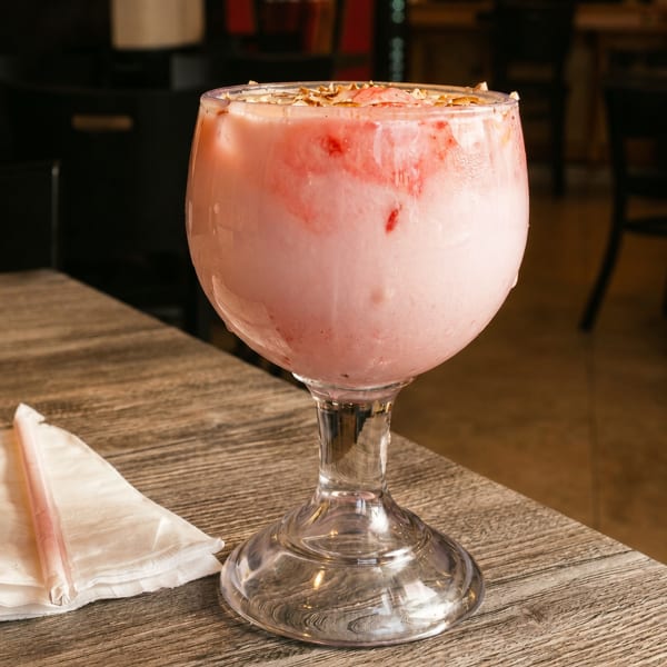 Pink strawberry milkshake in a large glass goblet with nuts on top, on a wooden table.